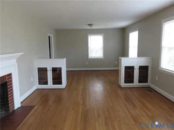 an empty room with wooden floor fireplace and windows