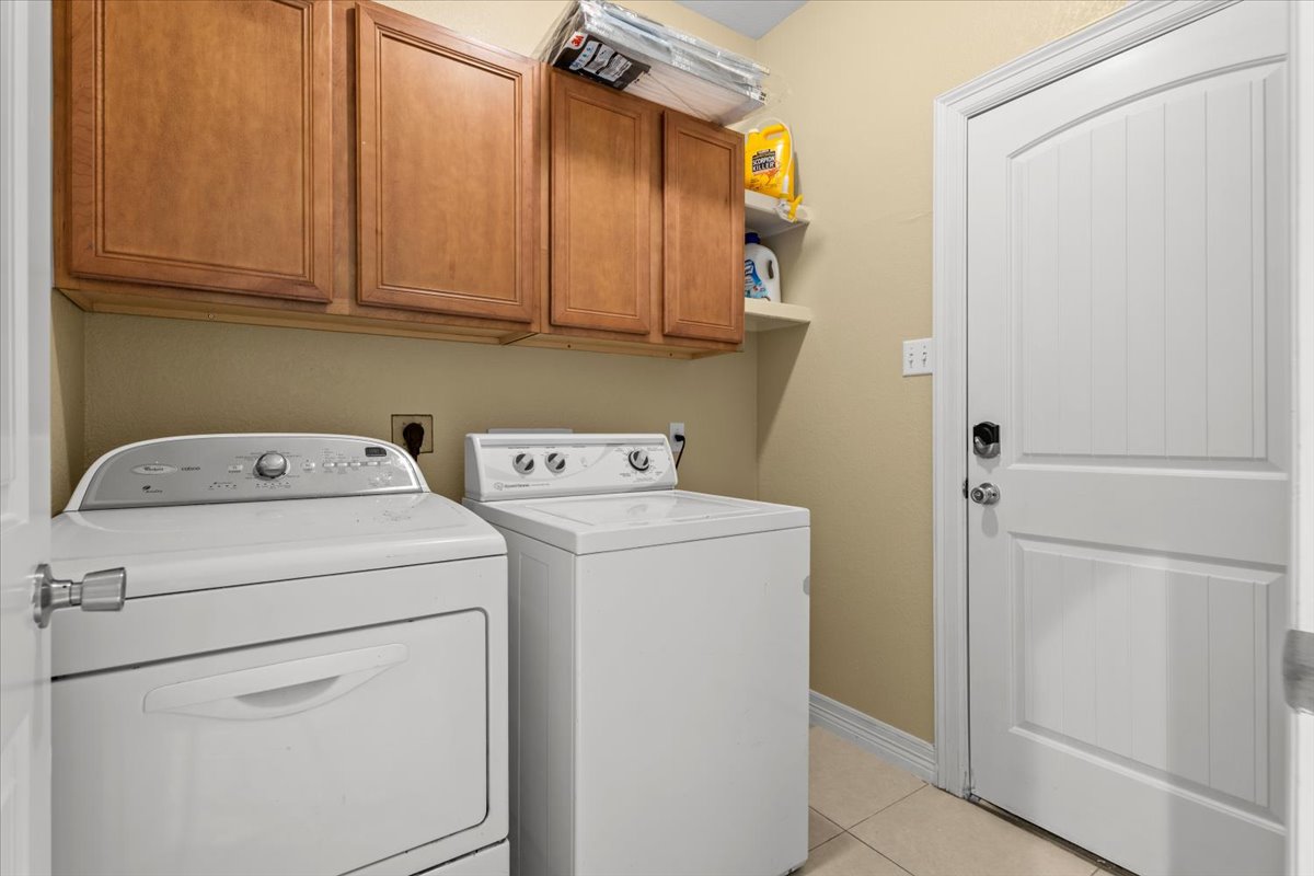 437 Balch Road Elgin, TX 78621 - Photo 11 of 37 Functional utility room featuring upper cabinetry and floor-level laundry machines for everyday convenience.
