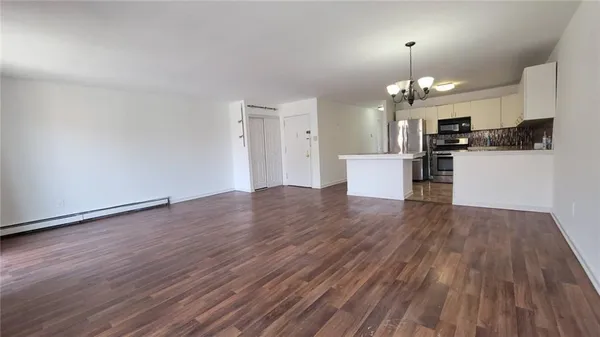 a view of an empty room and kitchen with wooden floor