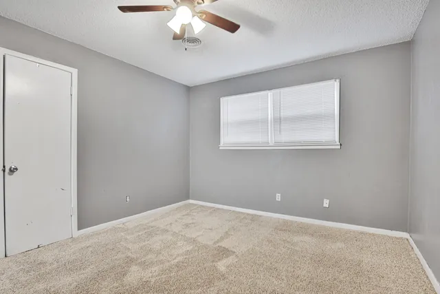 an empty room with a chandelier fan and windows