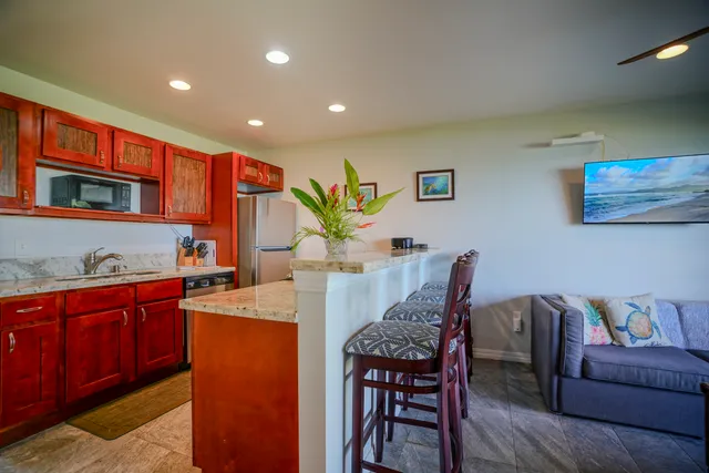 a living room with stainless steel appliances granite countertop furniture a couch a bookshelf a counter space and a sink