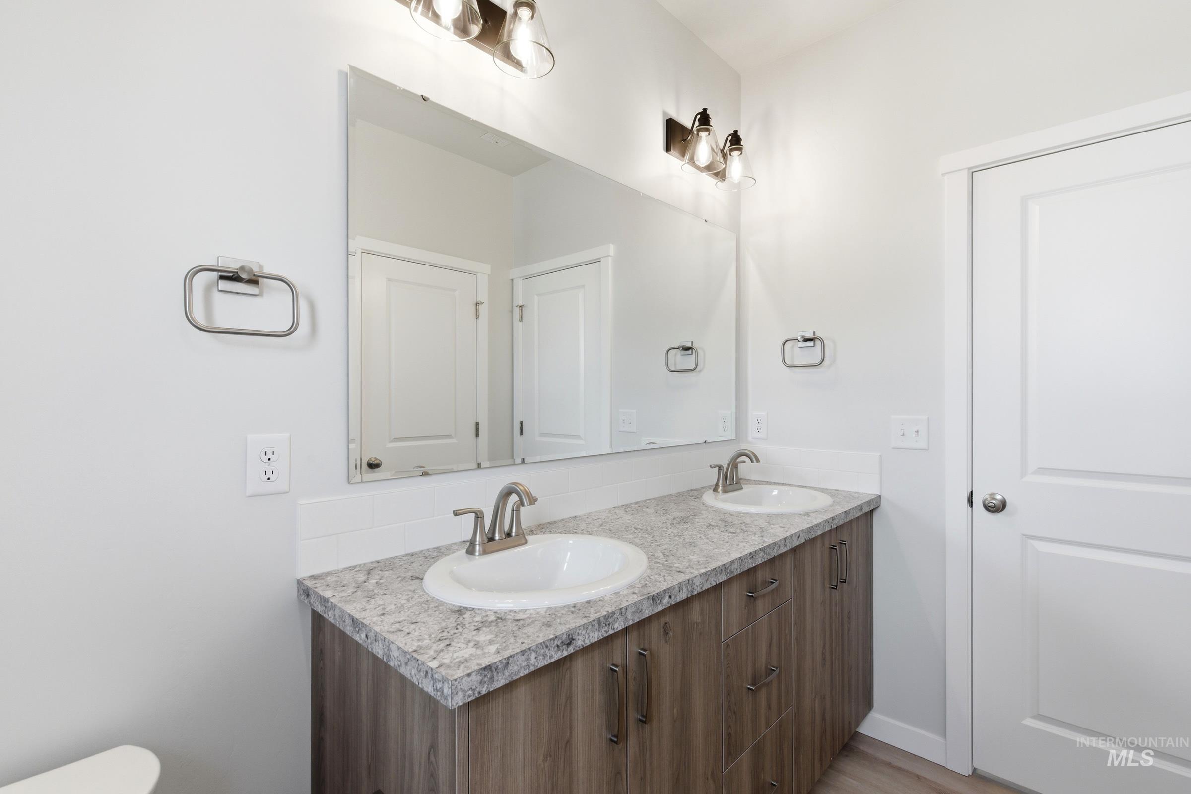 13663 Redway Court Caldwell, ID 83607 - Photo 23 of 32 Double vanity with wood-finish cabinetry, granite-look countertop, integrated sinks, and brushed nickel fixtures