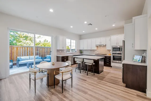 a kitchen with stainless steel appliances kitchen island granite countertop a table chairs sink and cabinets