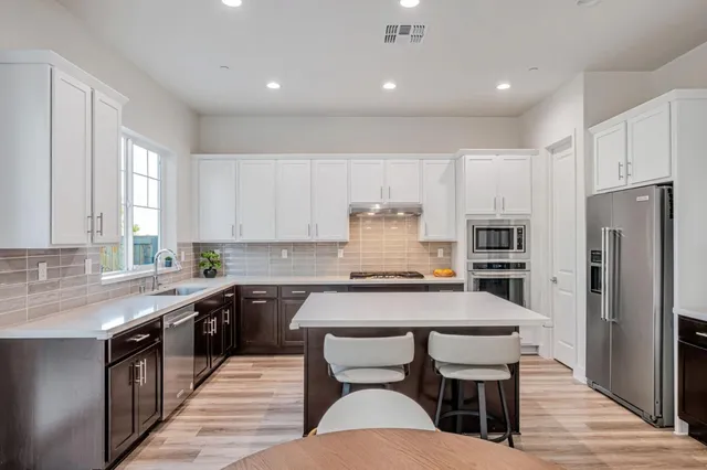 a kitchen with stainless steel appliances granite countertop a table chairs sink refrigerator and cabinets