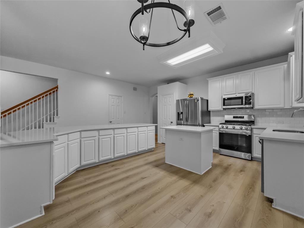 3008 Devlin Ridge Drive Plano, TX 75025 - Photo 7 of 24 Open-concept kitchen featuring white cabinetry, stainless steel appliances, a central island, light wood-finish flooring, and white countertops