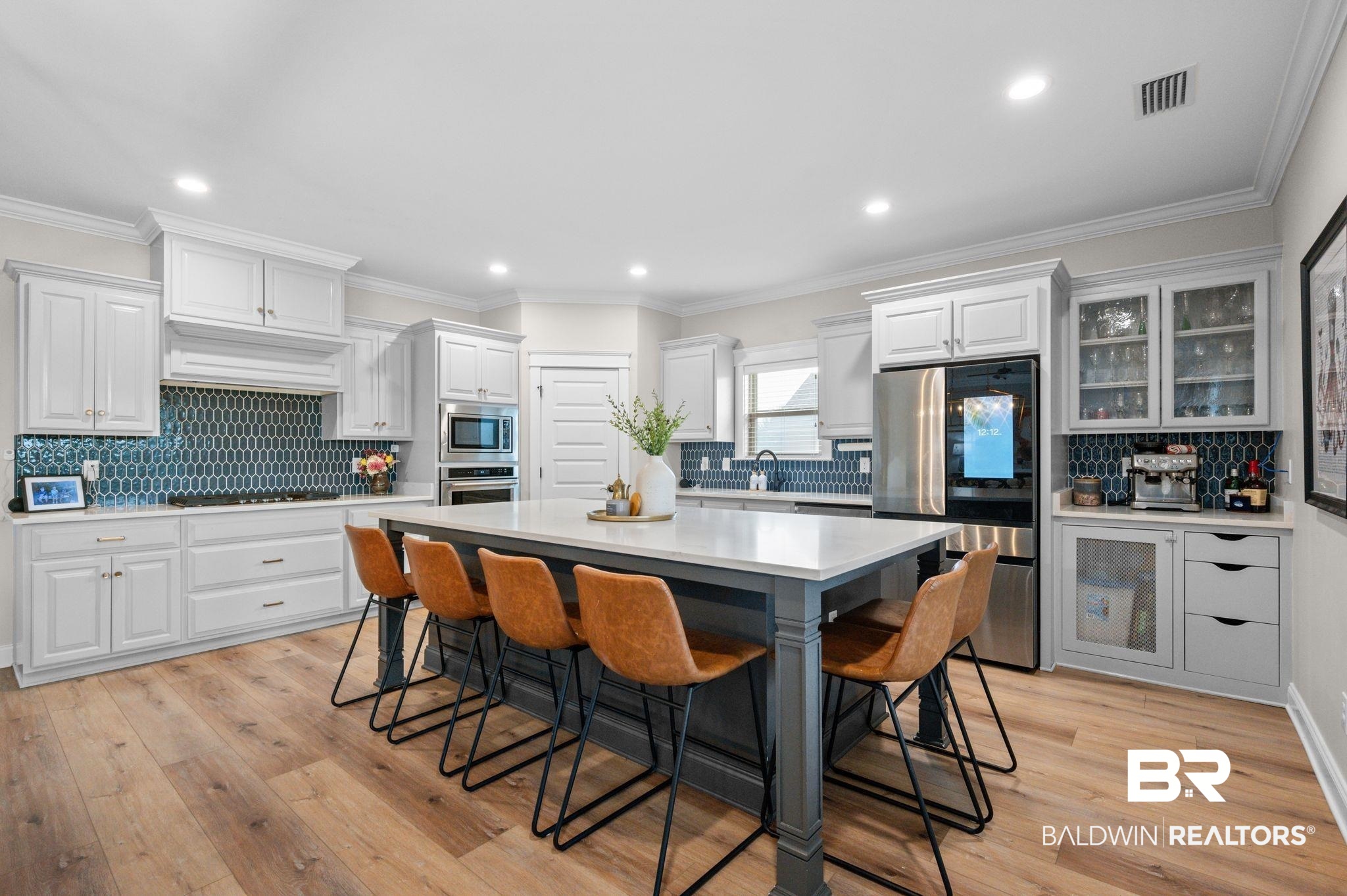 409 Fortune Drive Fairhope, AL 36532 - Photo 10 of 42 Kitchen featuring a central island with countertop seating, white shaker cabinetry, stainless steel appliances, a unique blue tile backsplash, and wood-finish flooring