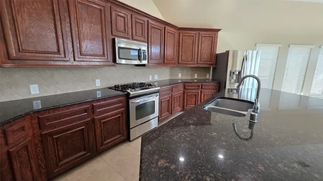 a kitchen with kitchen island granite countertop wooden cabinets a sink a stove a oven and a granite counter top