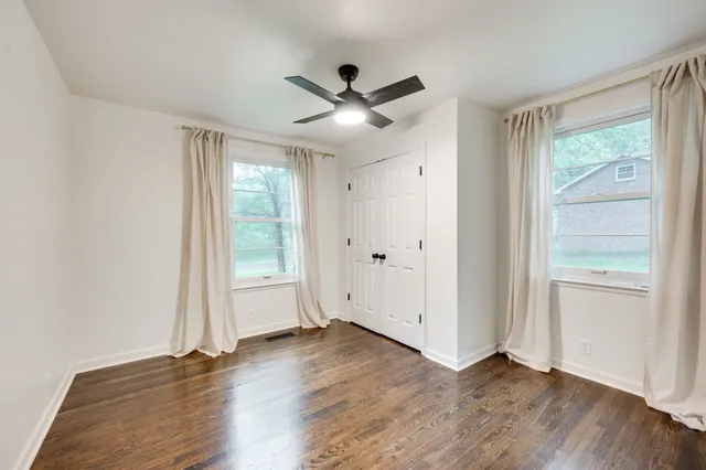 an empty room with wooden floor ceiling fan and windows