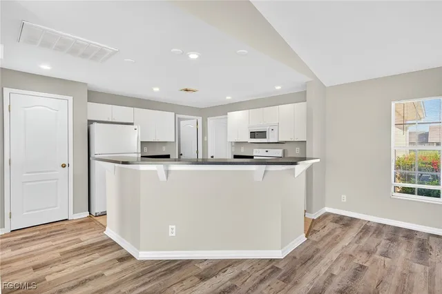 a view of kitchen with stainless steel appliances granite countertop a refrigerator sink and white cabinets with wooden floor