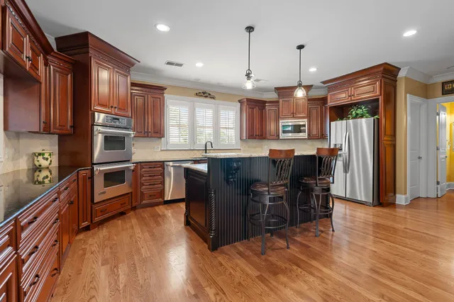 a kitchen with stainless steel appliances granite countertop a refrigerator a stove top oven a sink dishwasher a dining table and chairs with wooden floor