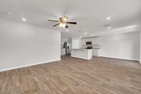 a view of empty room with wooden floor and kitchen view