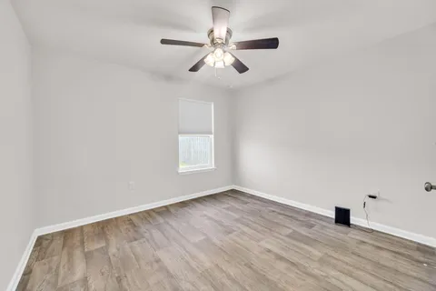 an empty room with wooden floor chandelier fan and windows