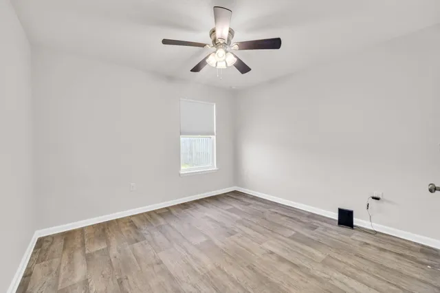 an empty room with wooden floor chandelier fan and windows