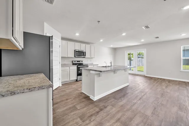 a large kitchen with a center island wooden floor stainless steel appliances and windows