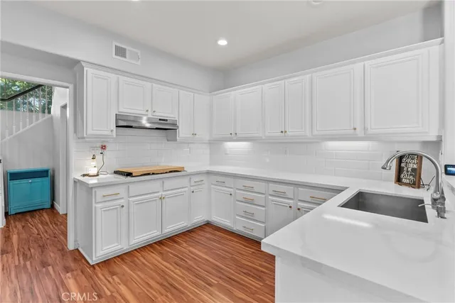 a kitchen with white cabinets white appliances sink and dishwasher with wooden floor
