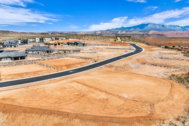 Undisclosed Address St. George, UT 84770 - Photo 2 of 11 Newly paved road winding through a developing neighborhood with graded lots, rock retaining walls, and distant mountain scenery