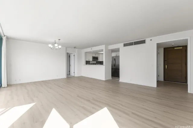 an empty room with wooden floor and kitchen view
