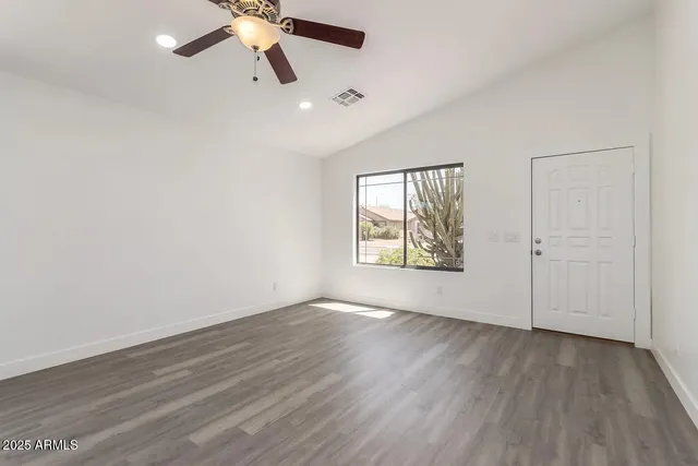 an empty room with wooden floor chandelier fan and windows