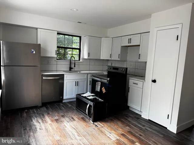 a kitchen with stainless steel appliances granite countertop a refrigerator a sink dishwasher a stove and white countertops with wooden floor