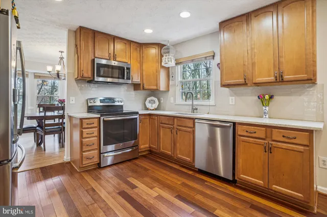 a kitchen with stainless steel appliances granite countertop wooden cabinets a sink a stove a dining table and chairs with wooden floor