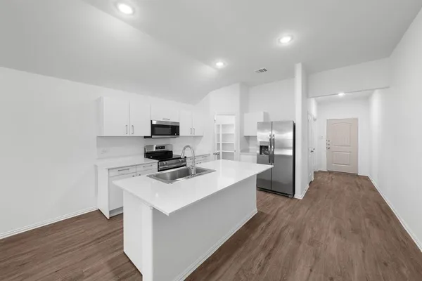 a kitchen with stainless steel appliances a refrigerator stove a sink and white cabinets with wooden floor