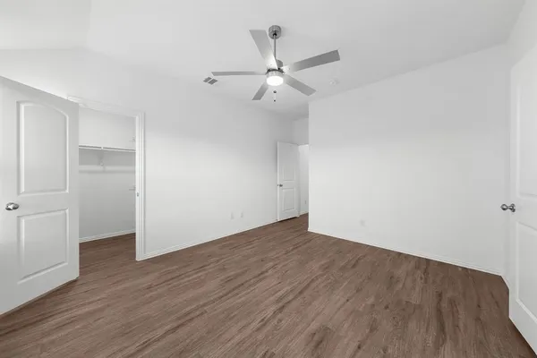 an empty room with wooden floor ceiling fan and windows