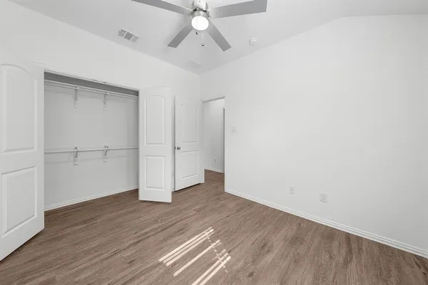an empty room with wooden floor closet and windows