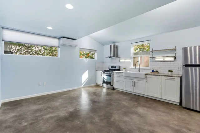 a kitchen with stainless steel appliances kitchen island granite countertop a dining table chairs and a refrigerator