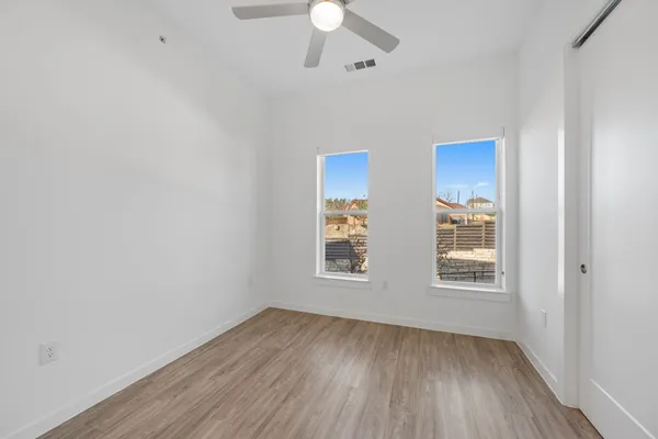 an empty room with wooden floor fan and windows