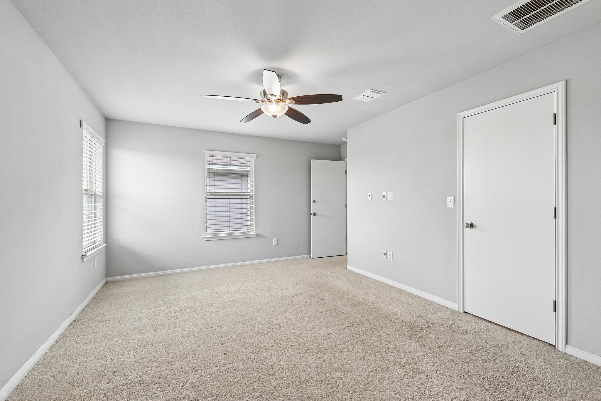 387 Guemal Road Buda, TX 78610 - Photo 31 of 39 Carpeted room with light grey walls, two windows featuring white blinds, white trim, a ceiling fan with integrated lighting, and two white doors