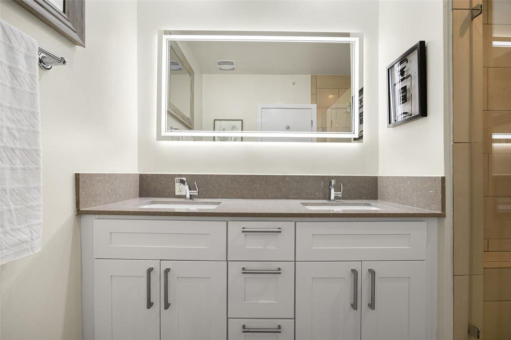 3922 Gilbert Avenue, Unit 214 Dallas, TX 75219 - Photo 13 of 27 Dual vanity with integrated sinks, a stone countertop, white shaker-style cabinetry, and a backlit mirror
