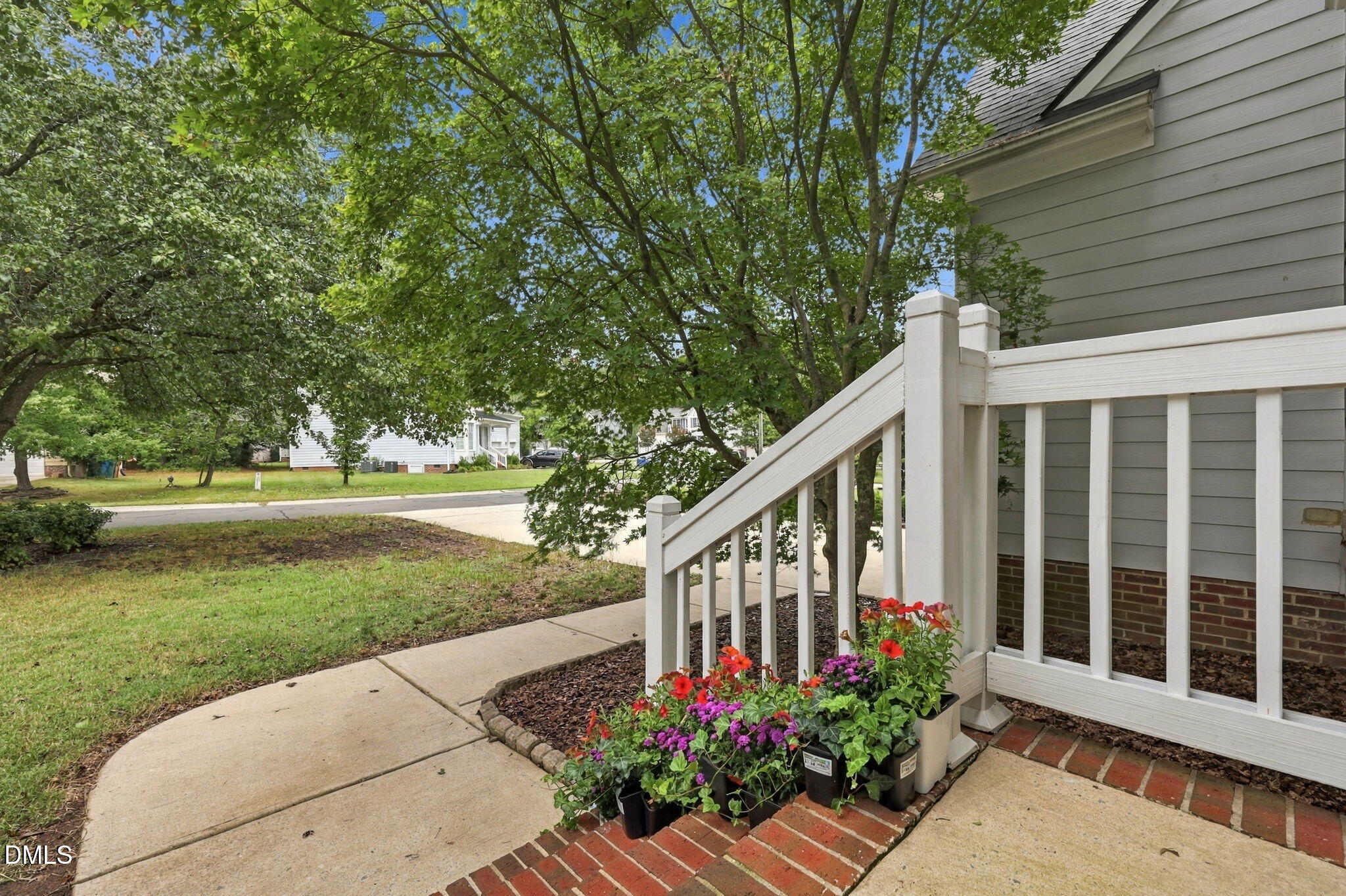 Welcoming front entry featuring a white-railed deck with brick base, complemented by seasonal flowering planters