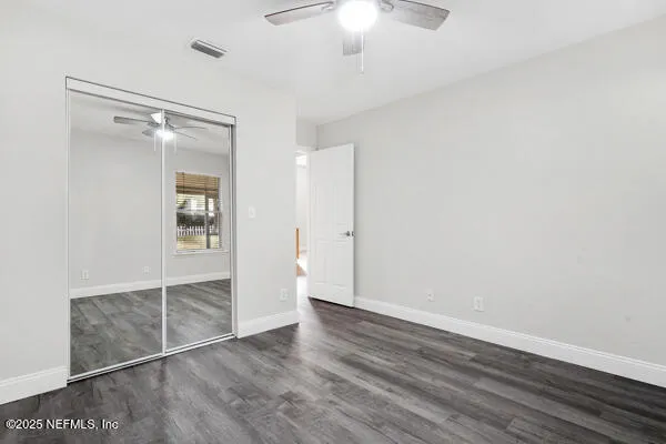 an empty room with wooden floor and way to kitchen