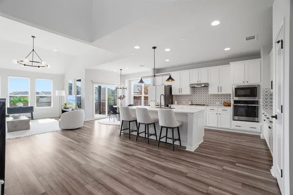 a kitchen with stainless steel appliances kitchen island granite countertop a dining table chairs and white cabinets next to a large window
