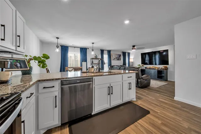 a kitchen with stainless steel appliances granite countertop a stove top oven a sink dishwasher and a refrigerator with wooden floor