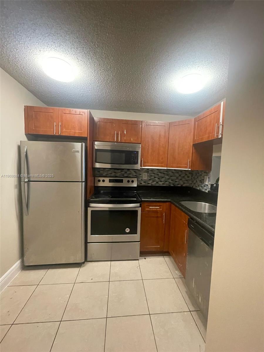 486 Northwest 165th Street, Unit B108 Miami, FL 33169 - Photo 2 of 8 a kitchen with granite countertop a refrigerator and a stove top oven