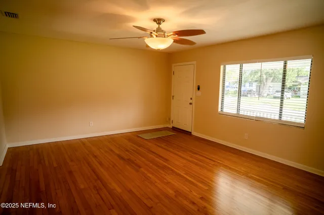 a view of an empty room with wooden floor and a window