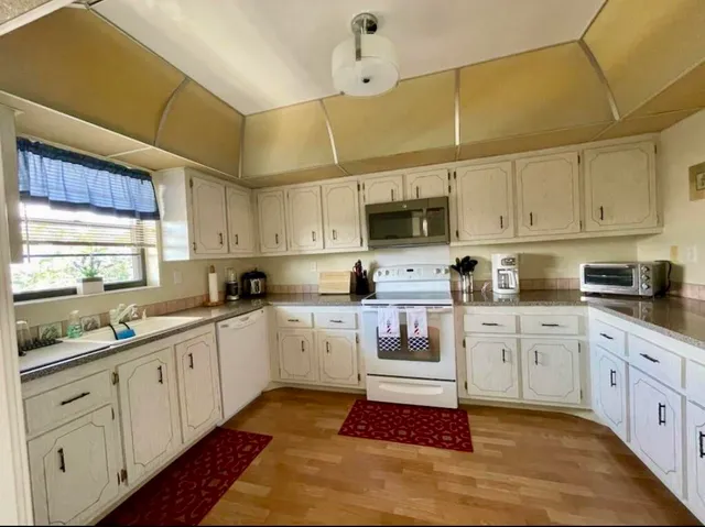 a kitchen with stainless steel appliances granite countertop a sink dishwasher a stove and white cabinets with wooden floor