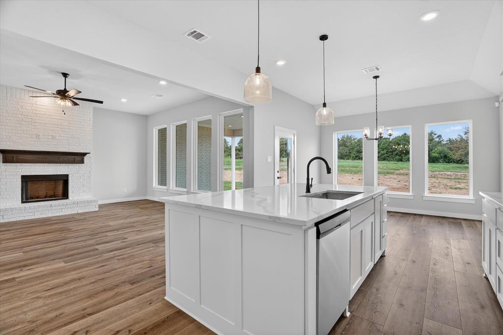 317 Skeen Peak Springtown, TX 76082 - Photo 6 of 31 Spacious open concept living area featuring a kitchen island with sink, white shaker cabinetry, stainless steel appliances, wood-finish flooring, and a whitewashed brick fireplace