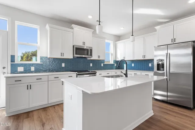a view of a kitchen with stainless steel appliances granite countertop a refrigerator a sink dishwasher a stove and white countertops with wooden floor