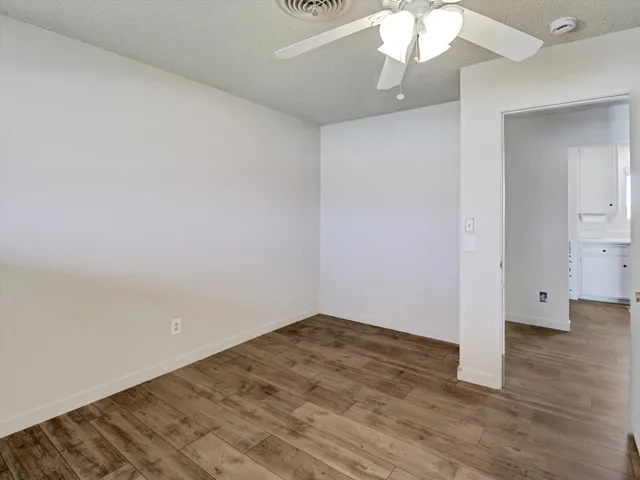 an empty room with wooden floor fan and windows