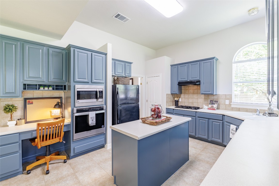 205 Ridge Run Court Georgetown, TX 78628 - Photo 19 of 40 a kitchen with kitchen island wooden cabinets a stove a sink a refrigerator and a window