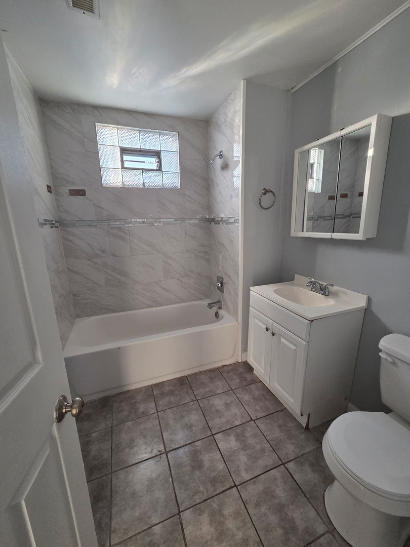 2704 East 77th Street, Unit 2 Chicago, IL 60649 - Photo 9 of 12 a bathroom with a granite countertop toilet a sink and bathtub