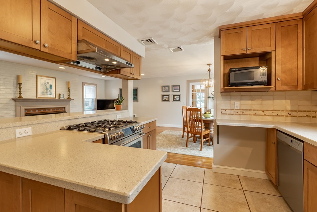 107 Oliver Road Waban, MA 02468 - Photo 9 of 32 a kitchen with stainless steel appliances granite countertop a stove top oven a sink a dining table and chairs with wooden floor