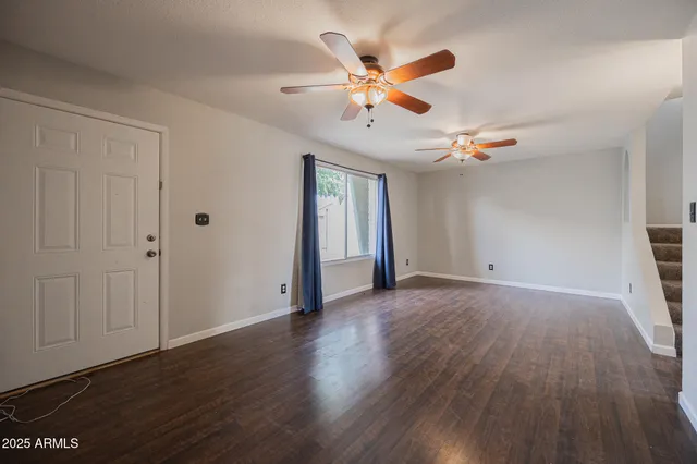 a view of an empty room with wooden floor and a ceiling fan