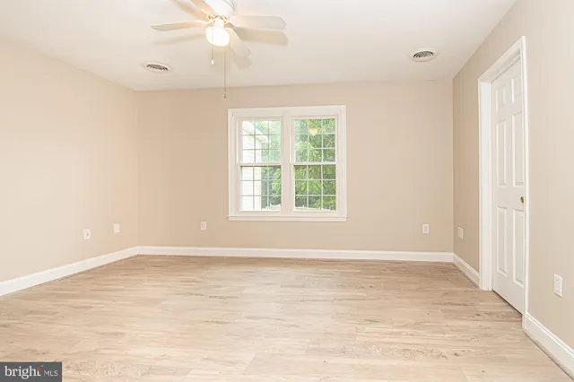 an empty room with wooden floor fan and windows