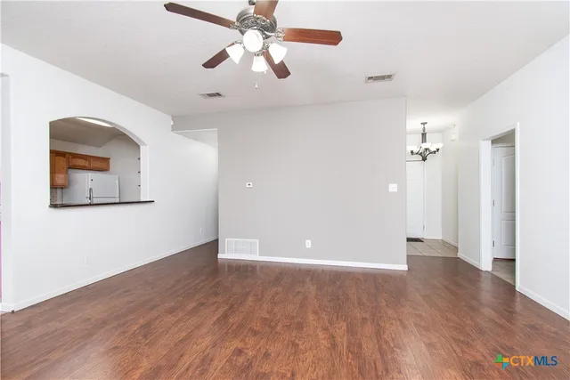 an empty room with wooden floor chandelier fan and windows