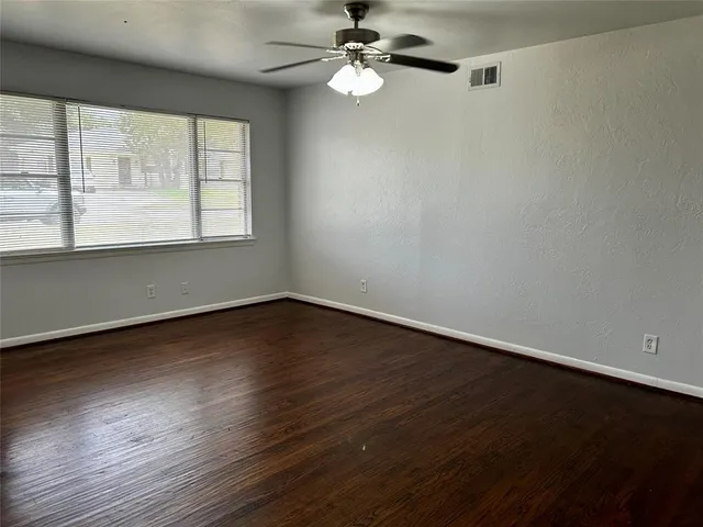 an empty room with wooden floor fan and windows