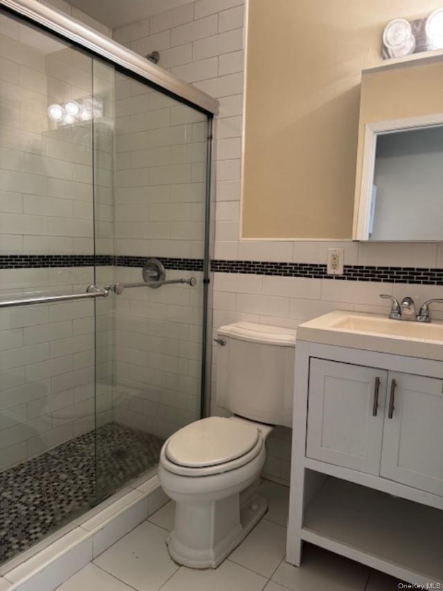 150-40 Tahoe Street, Unit 3C Queens, NY 11417 - Photo 14 of 18 Full bathroom featuring vanity, tile walls, light tile patterned floors, a shower stall, and wainscoting