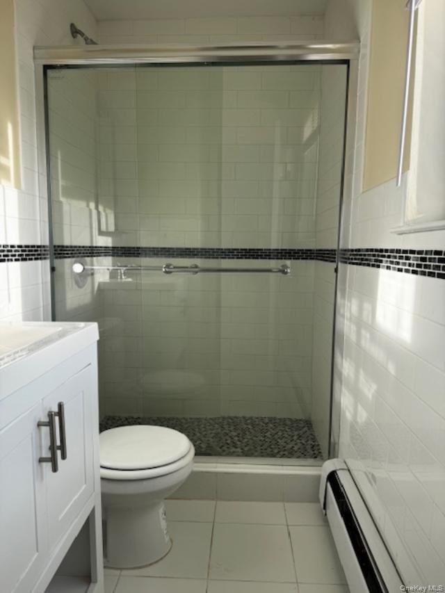 150-40 Tahoe Street, Unit 3C Queens, NY 11417 - Photo 15 of 18 Bathroom with a baseboard heating unit, light tile patterned flooring, vanity, a shower stall, and tile walls